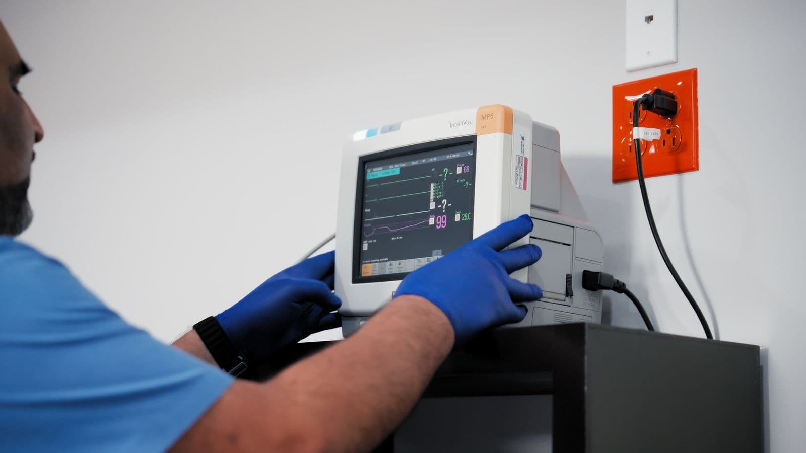 Manos con guantes ajustando un monitor de signos vitales